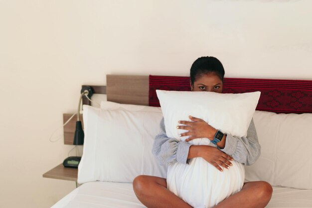 Portret van een mooie zwarte vrouw die haar lichaam bedekt met een kussen in de slaapkamer