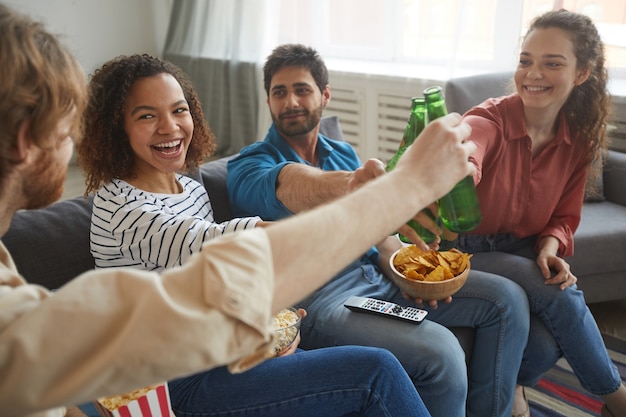 Portret van een multi-etnische groep vrienden rammelende bierflesjes tijdens het kijken naar Tv samen zittend op een comfortabele bank thuis