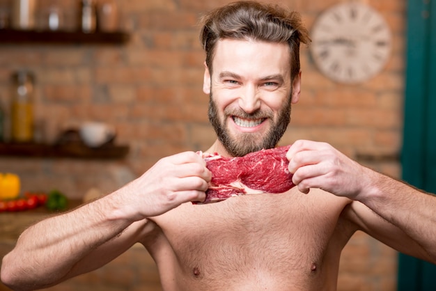 Portret van een naakte gespierde man die rauw vlees scheurt in de keuken