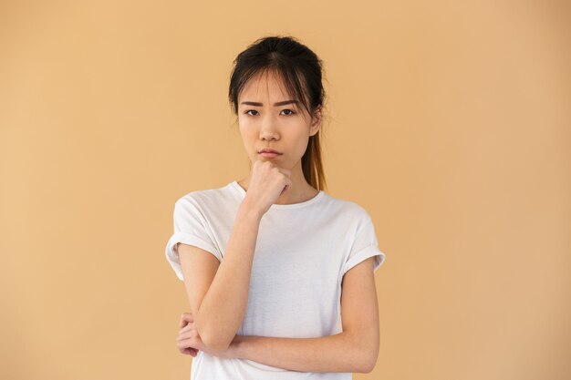 Portret van een obustige aziatische vrouw met een basic t-shirt aan de voorkant met een boze blik geïsoleerd over een beige muur in de studio