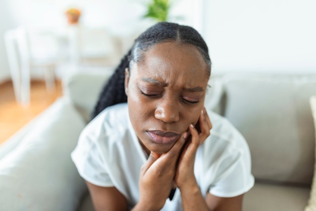 Portret van een ongelukkige Afro-Amerikaanse vrouw die thuis last heeft van kiespijn. Gezondheidszorg, tandheelkundige gezondheid en probleemconcept. Stock foto