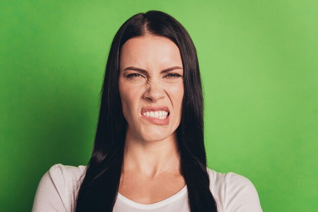 Portret van een ongelukkige blanke vrouw die een afkeer uitdrukt die over een groene achtergrond staat