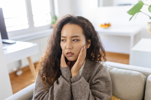 Foto portret van een ongelukkige jonge aziatische vrouw die thuis aan kiespijn lijdt gezondheidszorg tandheelkundige gezondheid en probleemconcept