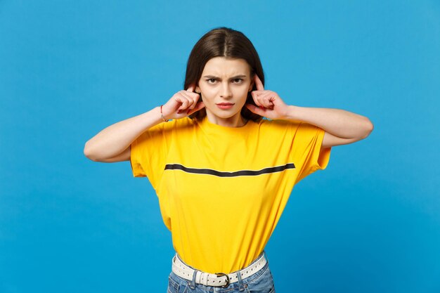 Foto portret van een ontevreden jonge vrouw in levendige vrijetijdskleding op zoek naar een camera, die oren bedekt met vingers geïsoleerd op een helderblauwe muurachtergrond in de studio. mensen levensstijl concept. bespotten kopie ruimte.