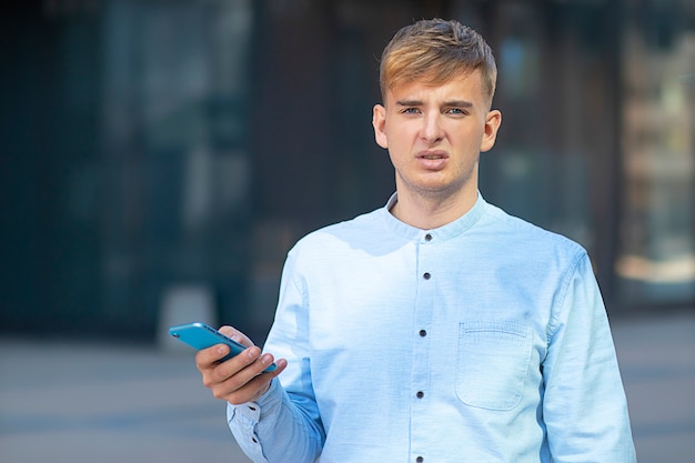 Portret van een ontevreden mannelijke zakenman die direct de camera bekijkt, die zijn mobiele smartphone in zijn hand houdt. Jonge boos student man.