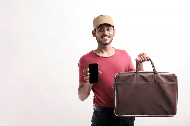 Portret van een opgewonden gelukkige jonge bezorger in pet die op een witte achtergrond staat. Kijkende camera met weergave van mobiele telefoon.