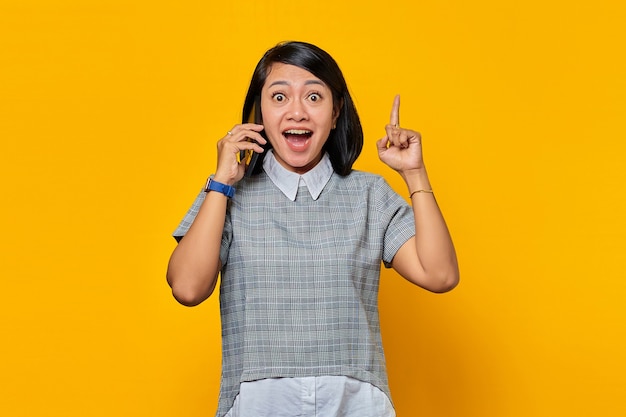 Portret van een opgewonden jonge aziatische vrouw die een mobiele telefoon vasthoudt en een vinger opsteekt omdat ze oplossingen heeft
