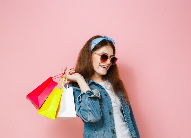 Portret van een opgewonden mooi meisje met zonnebril met boodschappentassen geïsoleerd over roze achtergrond