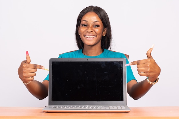 Portret van een opgewonden mooie jonge zwarte vrouw die naar haar laptopscherm wijst