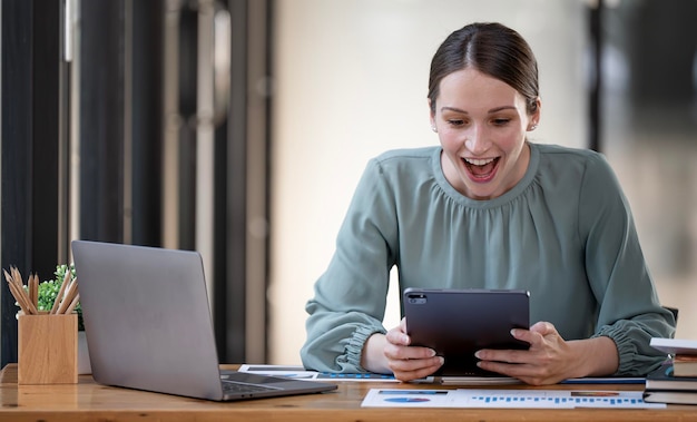 Portret van een opgewonden zakenvrouw die tevreden naar een digitale tablet kijkt terwijl ze aan haar bureau zit