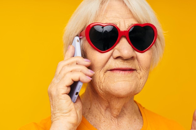Portret van een oude vriendelijke vrouw die een grimas op het gezicht stelt met een telefoon in de hand bijgesneden weergave