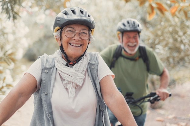 Portret van een oude vrouw die lacht en geniet van de natuur buiten op de fiets terwijl haar man lacht Headshot van een volwassen vrouw met een bril die zich gezond voelt Kijkend naar de camera