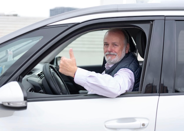 Portret van een oudere chauffeur in auto of taxi die zijn duim laat zien
