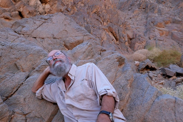 Foto portret van een oudere man die op een rots zit