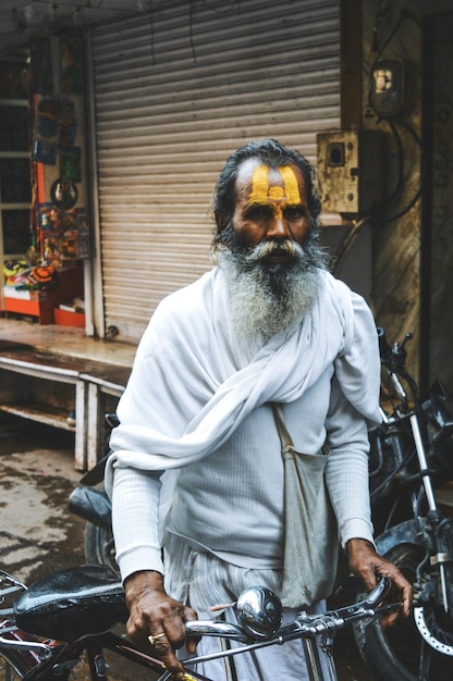 Portret van een oudere man in traditionele kleding met een fiets die op straat loopt