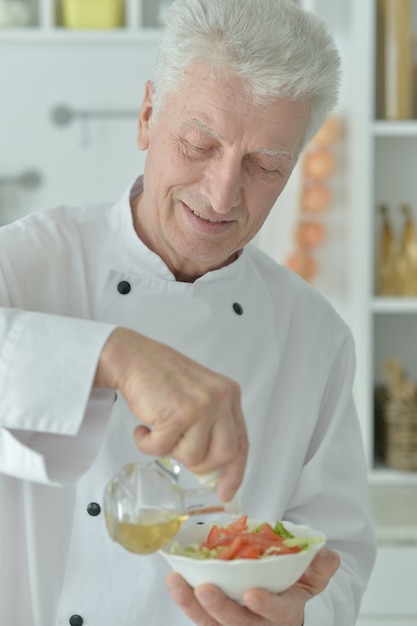 Portret van een oudere mannelijke chef-kok die salade kookt