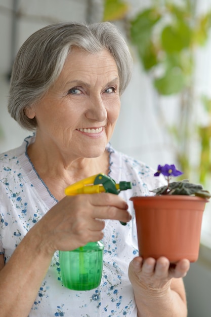 Portret van een oudere vrouw die de bloem water geeft