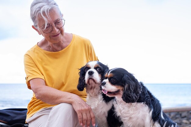 Portret van een oudere vrouw die dicht bij het strand zit met haar twee Cavalier King Charles honden