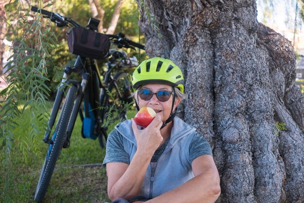 Foto portret van een oudere vrouw die een appel eet terwijl ze bij de boomstam zit