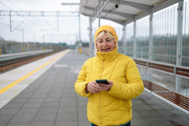 Foto portret van een oudere vrouw die een mobiele telefoon gebruikt terwijl ze op een tramstation wacht. hoogwaardige foto