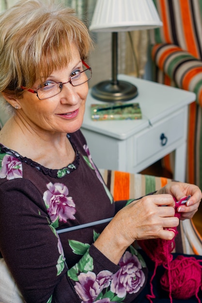 Portret van een oudere vrouw die thuis een wollen trui breit