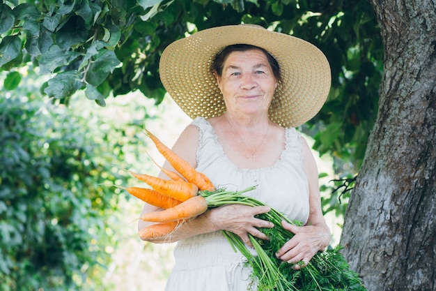 Portret van een oudere vrouw in een hoed met een wortel