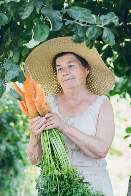 Portret van een oudere vrouw in een hoed met een wortel