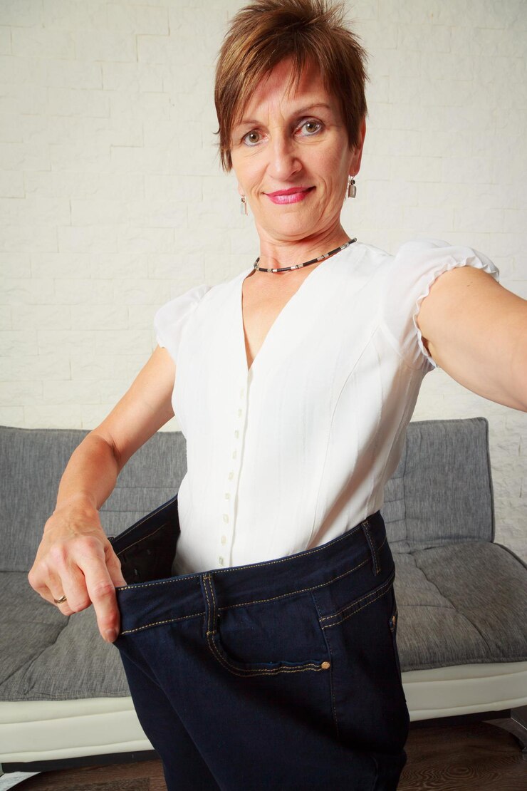 Foto portret van een oudere vrouw in een te grote broek die thuis tegen de muur staat