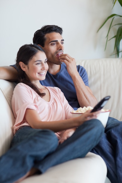 Portret van een paar dat TV let terwijl het eten van popcorn