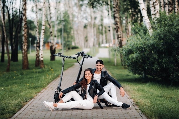 Portret van een paar zitten in de buurt van elektrische scooters, samen genieten van tijd in de natuur, twee geliefden op elektrische scooters