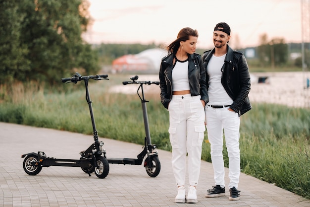 Portret van een paar zitten in de buurt van elektrische scooters, samen genieten van tijd in de natuur, twee geliefden op elektrische scooters