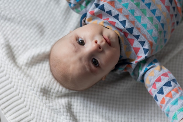 Portret van een pasgeboren baby in een gekleurd rompertje liggend op zijn rug op een gebreide witte deken