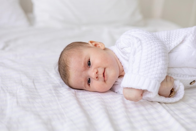 Portret van een pasgeboren baby in een wieg in een witte warme jumpsuit op een wit geïsoleerd katoenen bed, schattige babyclose-up