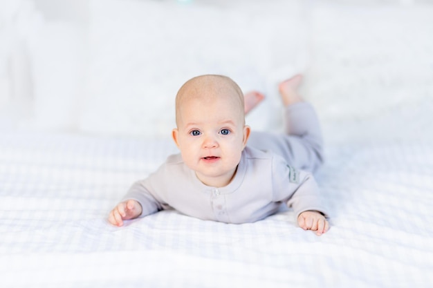 Portret van een pasgeboren babymeisje in een katoenen pak op een wit bed dat thuis ligt en glimlacht