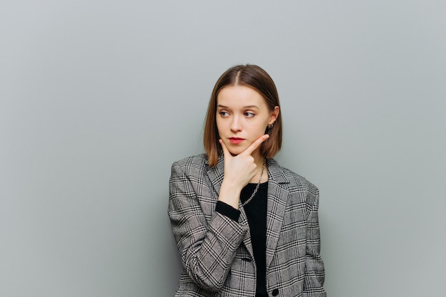 Portret van een peinzende jonge vrouw in slimme vrijetijdskleding op een grijze achtergrond