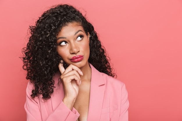 Portret van een peinzende mooie mooie jonge vrouw die zomerkleding draagt die geïsoleerd over roze muur staat