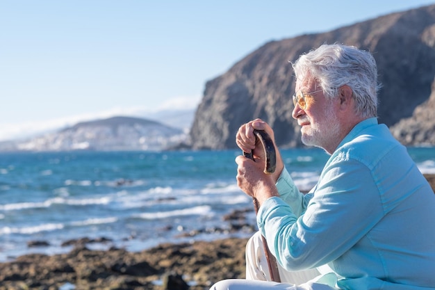 Portret van een peinzende volwassen bebaarde senior man die op het strand rust, hand in hand op een wandelstok