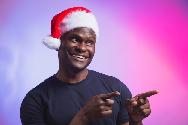 Portret van een positieve Afro-Amerikaanse glimlachende man in een kerstmuts en een casual t-shirt op kleurrijk