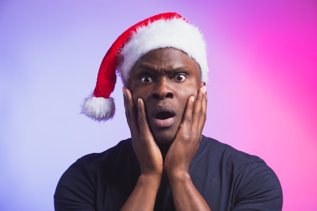 Portret van een positieve afro-amerikaanse glimlachende man in een kerstmuts en een casual t-shirt op kleurrijk