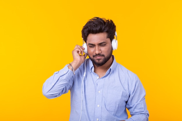 Portret van een positieve jonge Indiase man met een baard, luisteren naar een audioboek op gele ruimte