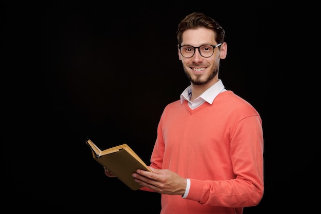 Portret van een positieve jonge man in een oranje trui die koffie drinkt om tegen zwarte achtergrond te gaan