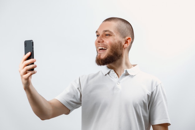 Portret van een positieve knappe bebaarde man in een wit t-shirt praten over video-oproep met behulp van een smartphone