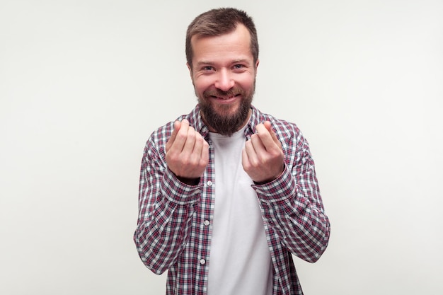 Portret van een positieve, sluwe, bebaarde man in een casual geruit hemd met geldgebaar en grijns, illegale winst plannend, wat contant geld nodig, betaling. indoor studio-opname geïsoleerd op een witte achtergrond