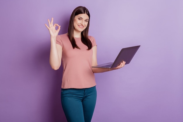 Portret van een positieve succesvolle vrouw, een gelukkige positieve glimlach, laat zien dat het goed is, gebruik een laptop geïsoleerd over een violette kleurachtergrond