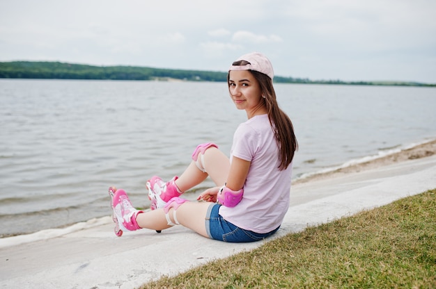 Portret van een prachtige jonge vrouw in vrijetijdskleding en pet zittend op de grond naast het meer.