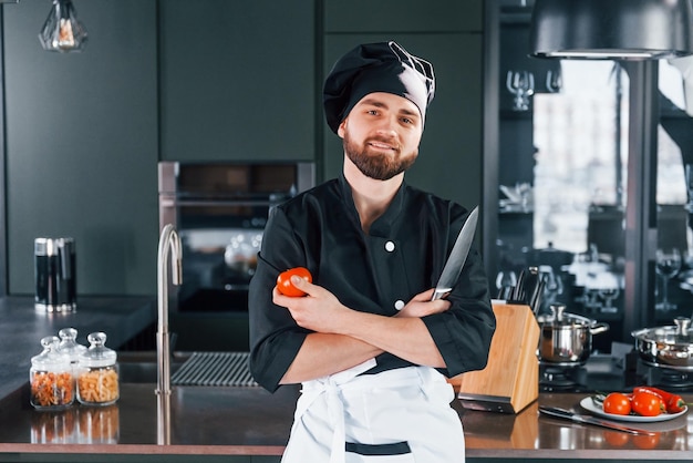 Portret van een professionele jonge chef-kok in uniform die poseert voor de camera in de keuken