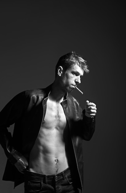 Portret van een rebellentype in een klassiek leren jack met een sigaret in de mond tegen een donkere achtergrond
