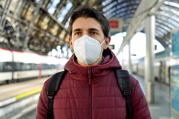 Portret van een reiziger die een medisch gezichtsmasker van KN95 FFP2 draagt met een rijdende trein op de achtergrond op het treinstation