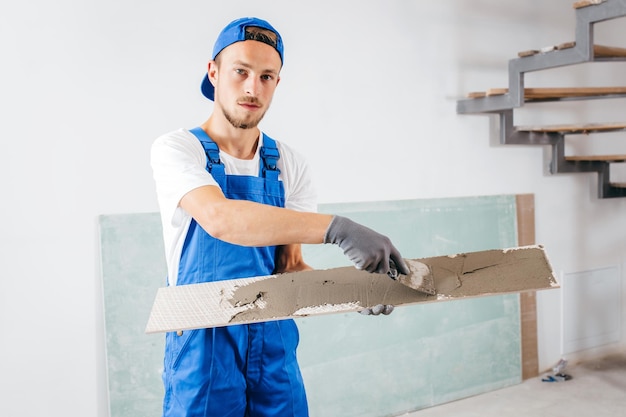 Portret van een reparateur in grijze handschoenen en een speciaal uniform dat cement op tegels in een nieuw huis legt