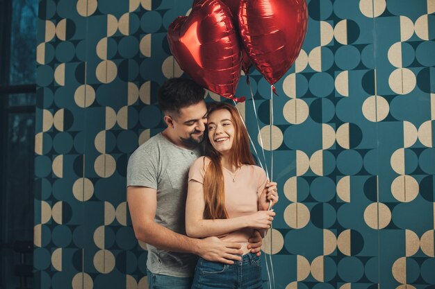 Portret van een roodharige vrouw met hartvormige luchtballonnen en haar vriendje poseren terwijl ze lacht...